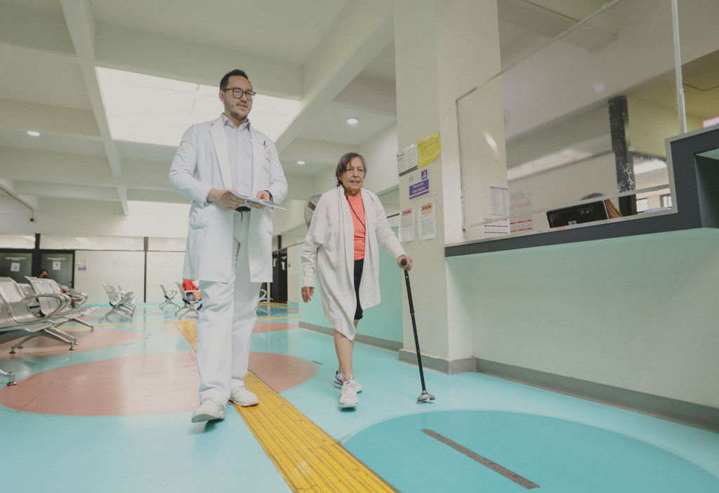 Paciente adulta mayor camina con bastón junto a su médico