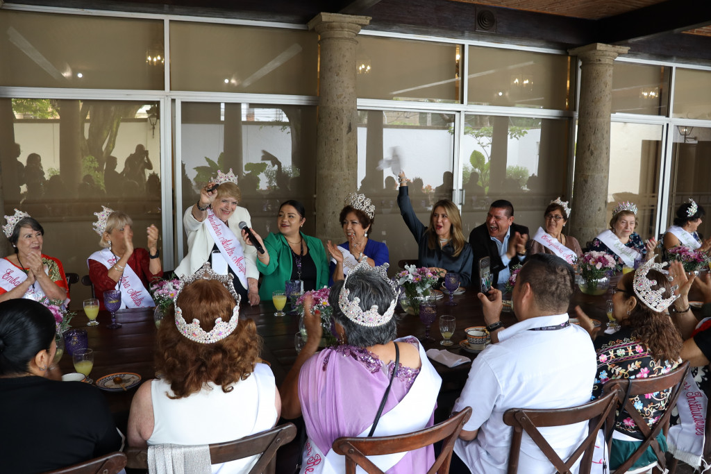 Candidatas sentadas a la mesa junto a autoridades aplauden a una compañera