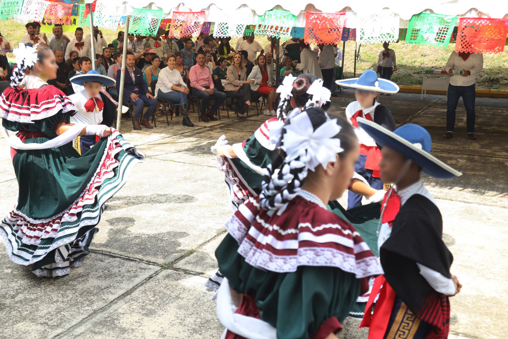 Ballet folclórico de Cien Corazones bailan mientras autoriddes y asistentes los observan al fondo