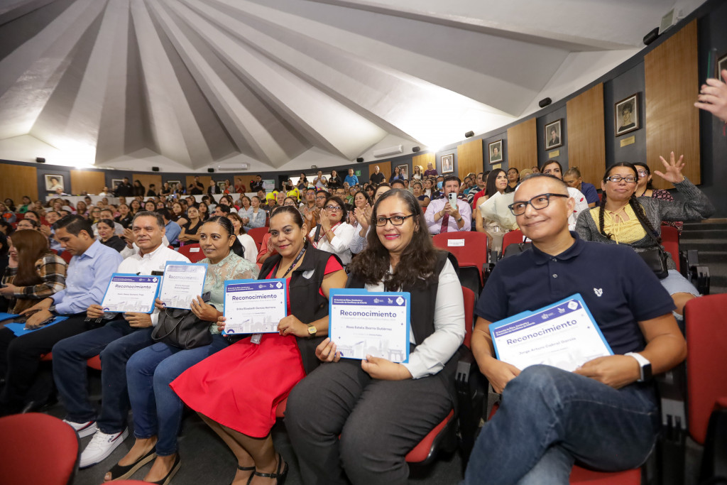 Servidores públicos sentados en primera fila sostienen su reconociemiento en la mano