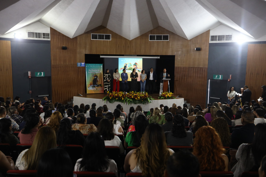 Autoridades al fondo en el presidium hablan frente a las y los asistentes