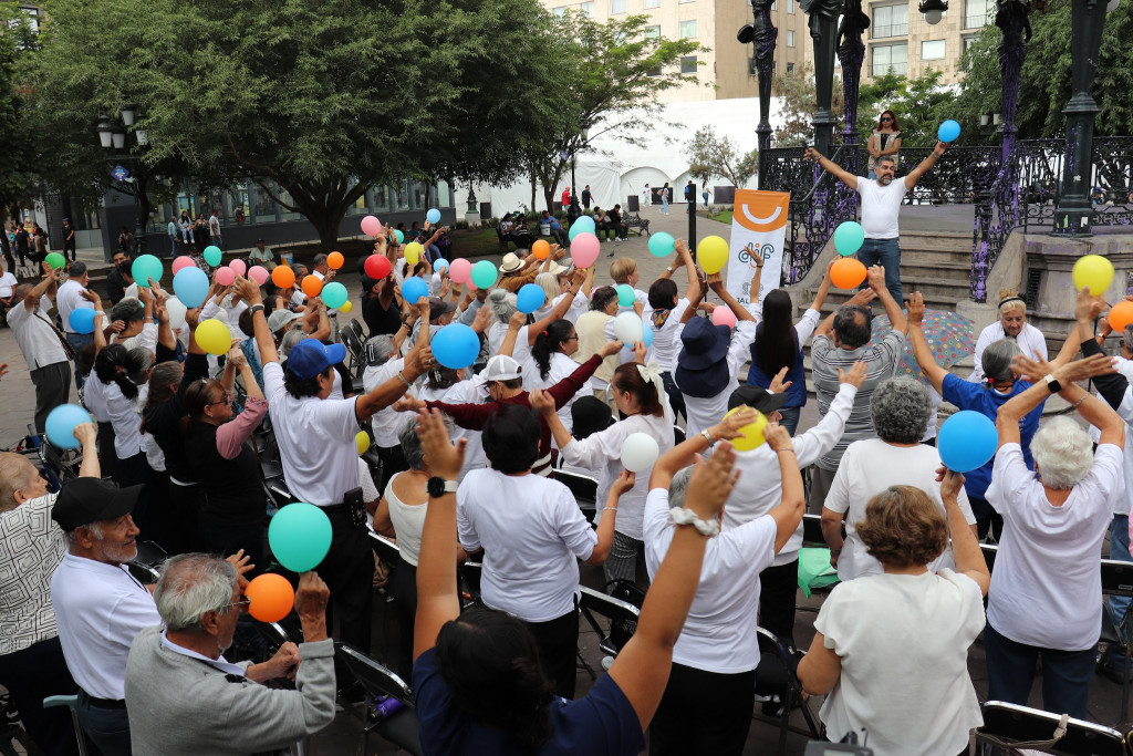 Personas adultas mayores activas con globos de colores frente al kiosco de Plaza de Armas
