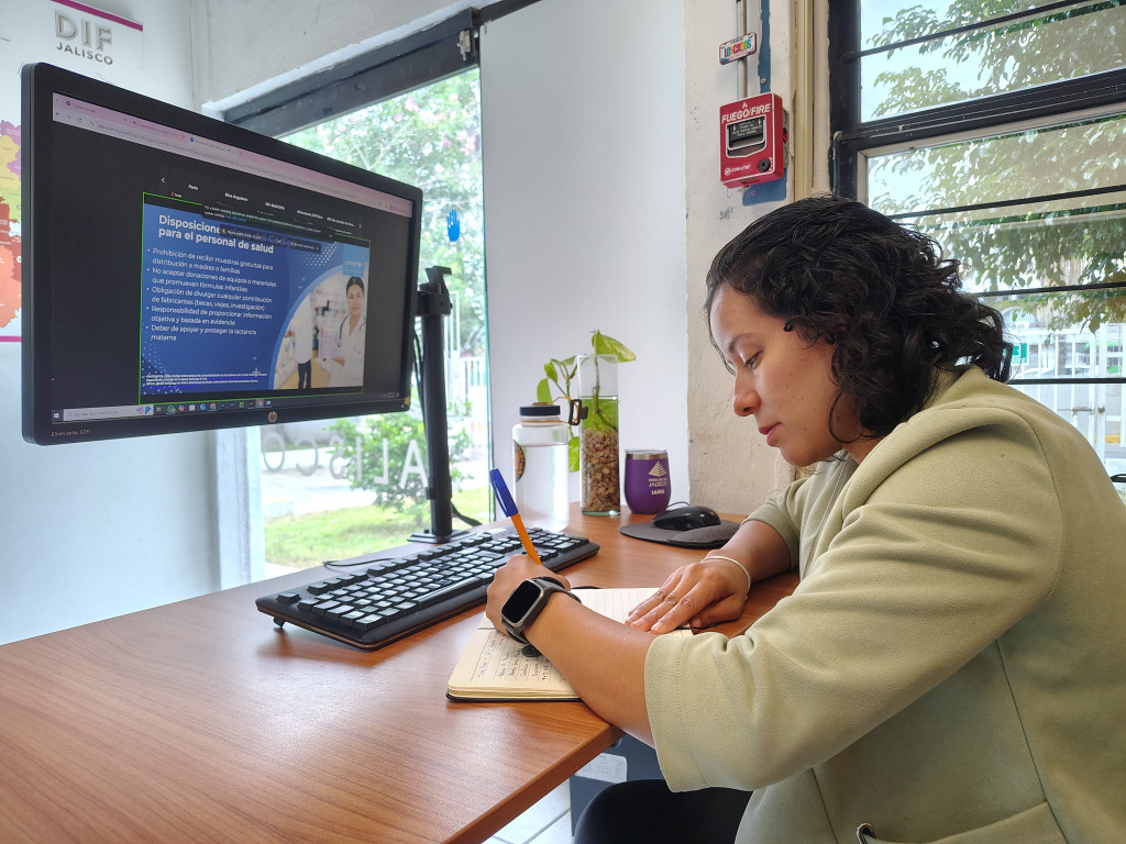 Colaboradora tomando nota sobre la comferencia , frente a ella una pantalla de pc con el tema