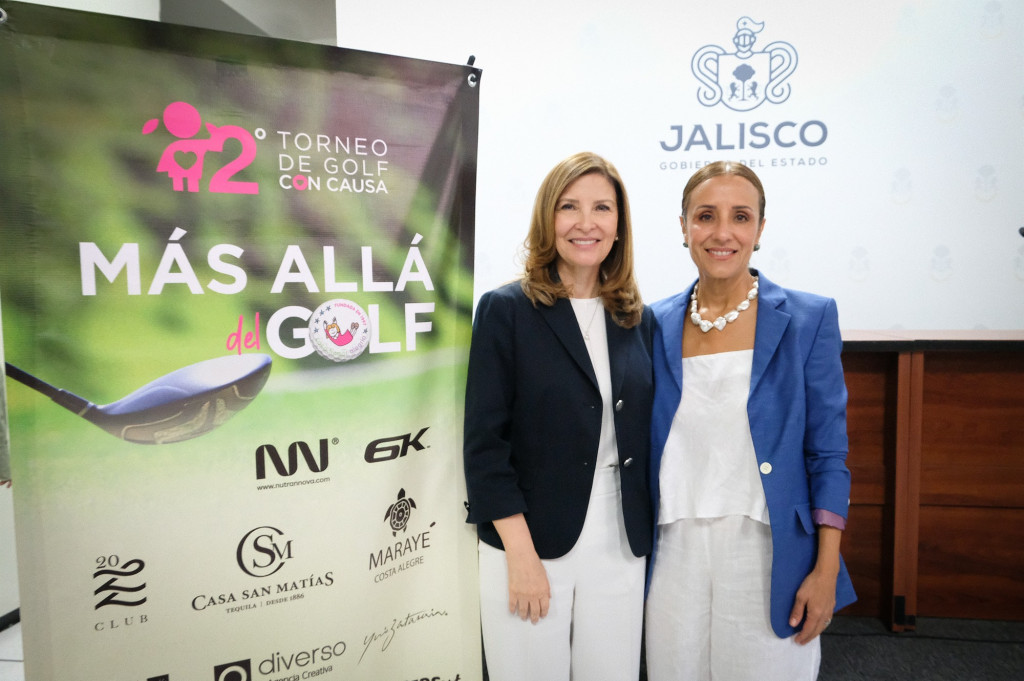 Maye Vila y Carmen Villarreal de pie junto al banner oficial con la imagen del evento