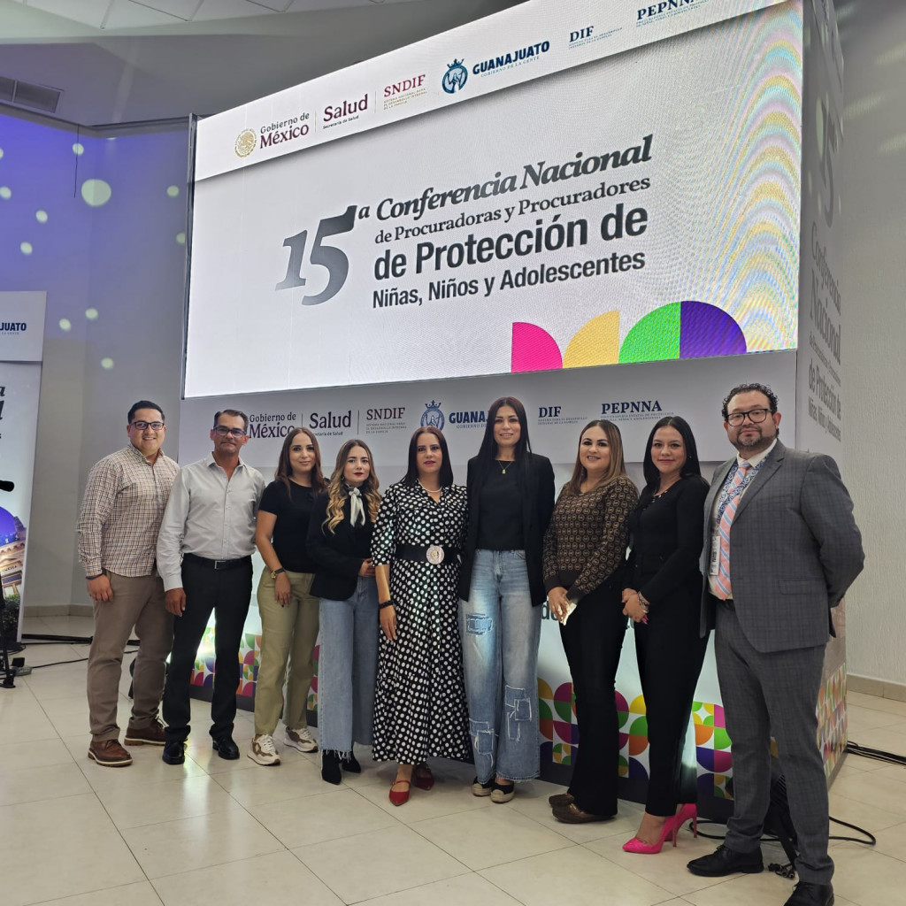 Procuradora Sandra Trelles junto a la Comitiva de Jalisco, al fondo de observa una pantalla con el nombre del evento