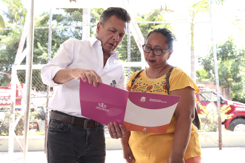 Gobernador Pablo Lemus entrega lee la carpeta que tiene al interior el cheque junto a la beneficiaria
