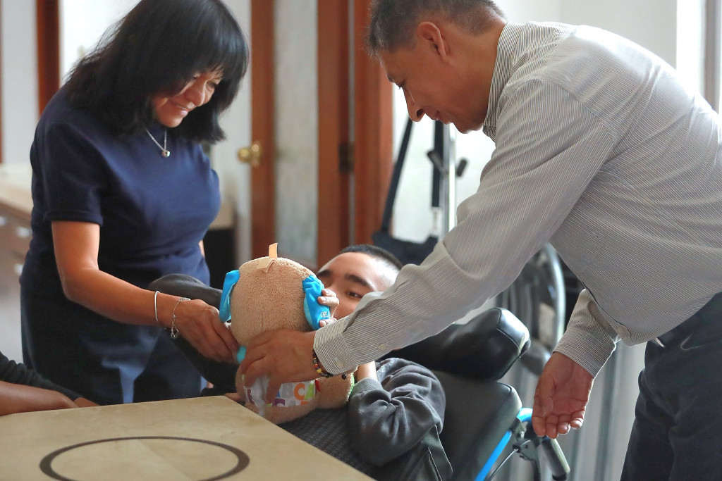 Madre y Padre le enseñan un peluche a su hijo Pío quien se encuentra en Silla de ruedas