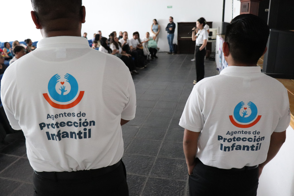 Dos agentes de espaldas con logotipo impreso en sus playeras al fondo de observa la capacitación instruida al personal municipal