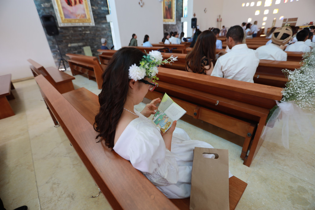 Niña en la ultima banca de la iglesia observa su libro ilustrado al fondo se observan las demá bancas con residentes y sus padrinos